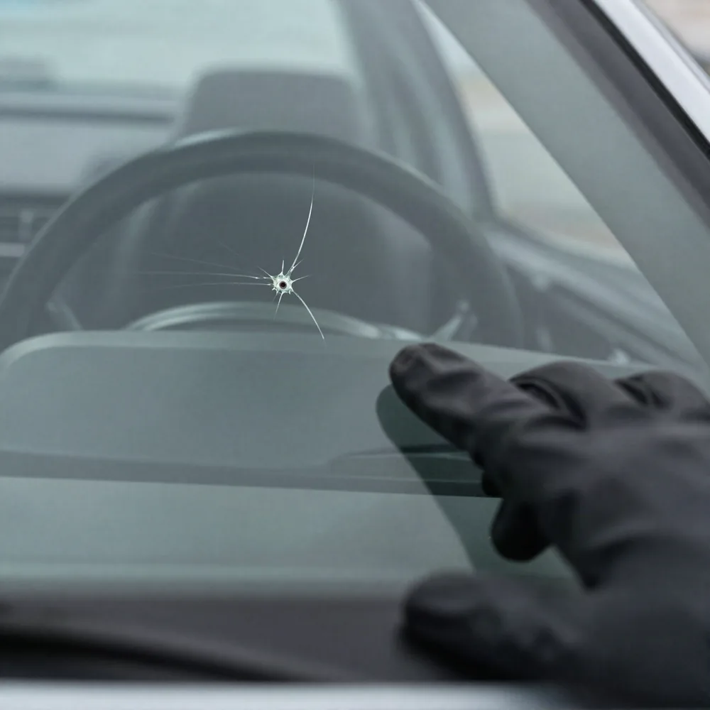 A bullseye stone chip with crack legs spreading through a car windshield, dashboard visible behind the glass